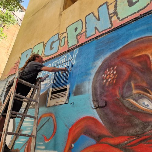 L'artiste Poasson in situ à l'Ostaria, restaurant dans le quartier du panier à Marseille, fresque réalisée pour la terrasse au mois de juillet 2023, à l'aérosol. Les fonds marins et un clin d'oeil à Hugo pratt et son personnage Corto maltese. Street-Art et Graffiti